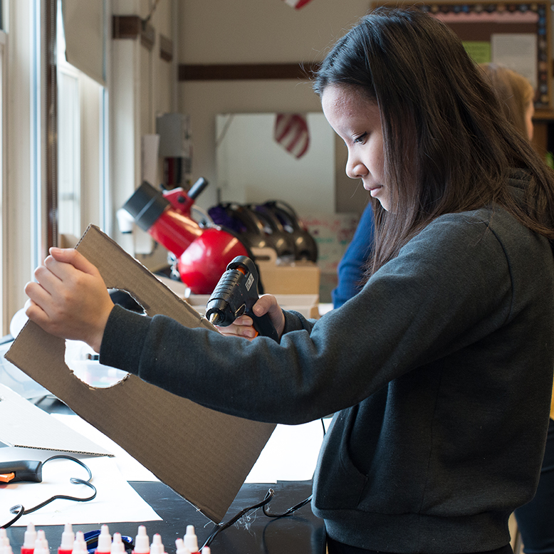 A student using a glue gun to stick her cardboard prototype together.
