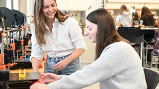 A university lecturer working with a student on CAD modelling.
