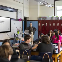 A group of students in a classroom with a representative of the James Dyson Foundation who's hosting a prototyping workshop with them.