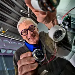 Sir James Dyson looking through a glass table holding machine parts.