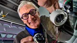Sir James Dyson looking through a glass table holding machine parts.