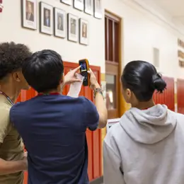 Three students using the air quality monitoring device in the hallway of their school.